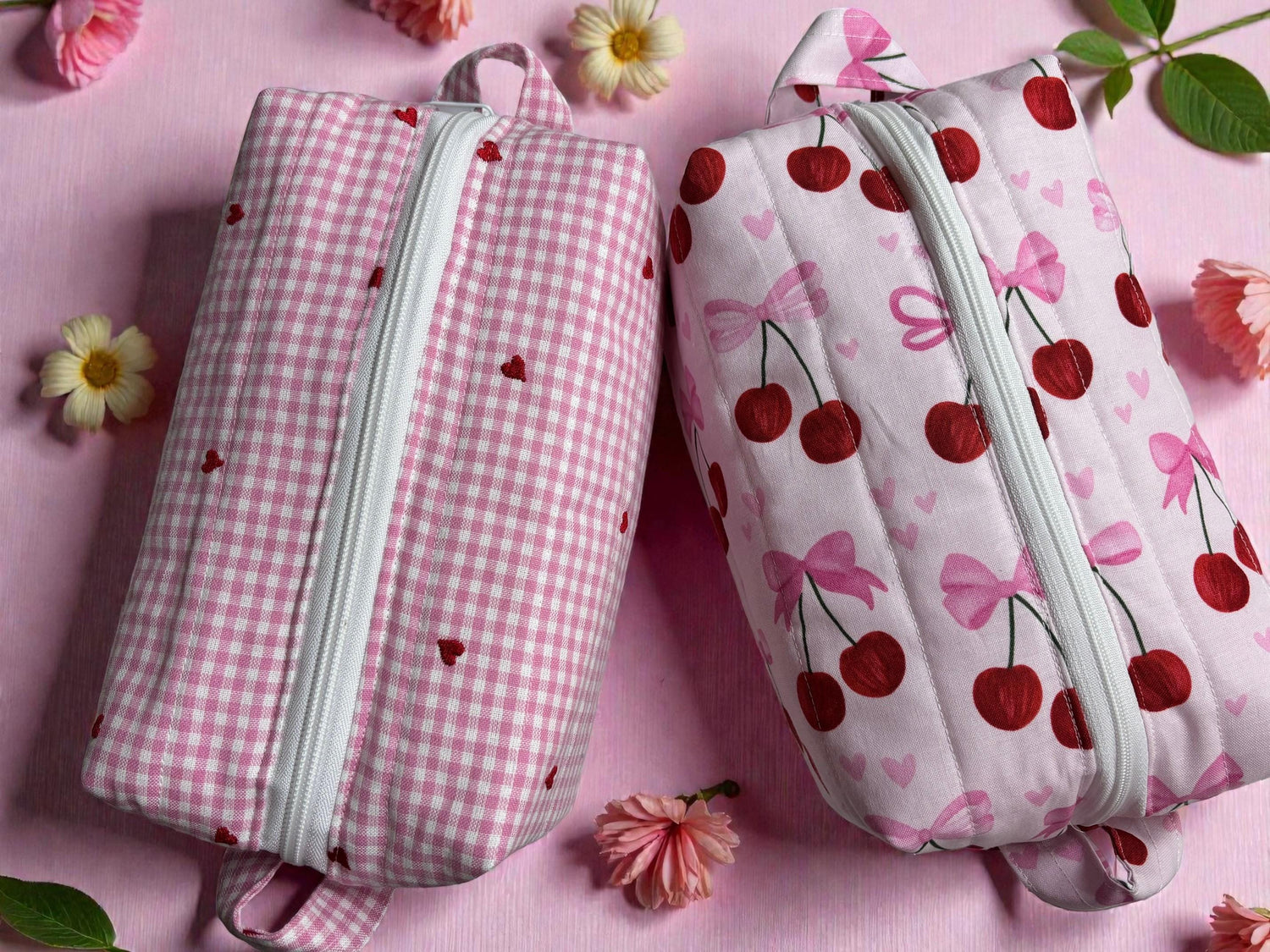 Two handmade quilted pouches with zippers; pink gingham with hearts and a cherry-bow pattern.